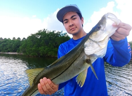 Person in front of Tampa Bay holding a green fish that was caught