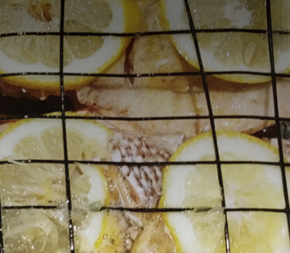 Fish grilling over a flame with a slice of lemon on top